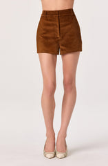 A person is wearing high-waisted brown shorts made of a soft, textured fabric, paired with light-colored pointed-toe shoes. The shorts feature a waistband with belt loops and a front zipper closure.