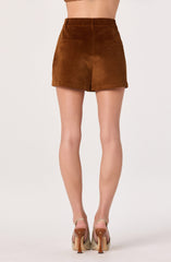 A person is wearing a high-waisted, brown suede mini skirt with belt loops and side pockets. They are also wearing beige high-heeled shoes with ankle straps.