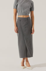 A person is wearing a loose-fitting, short-sleeved, grey crop top with a rounded neckline, paired with high-waisted, grey wide-leg trousers featuring thin vertical white pinstripes and a single button on the waistband. They are also wearing white pointed-toe high heels.