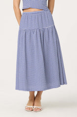 A woman is wearing a matching two-piece outfit with a blue and white small gingham check pattern. The top is sleeveless and cropped, ending just above the waist. The matching skirt is high-waisted, A-line, and reaches down to the ankles with a tiered, gathered design. She is also wearing white open-toe sandals with a bow detail on the front.