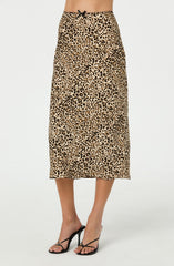 A woman is wearing a long, high-waisted skirt with a leopard print pattern in shades of tan and black, featuring a small black bow at the waistband. She pairs the skirt with black high-heeled sandals.