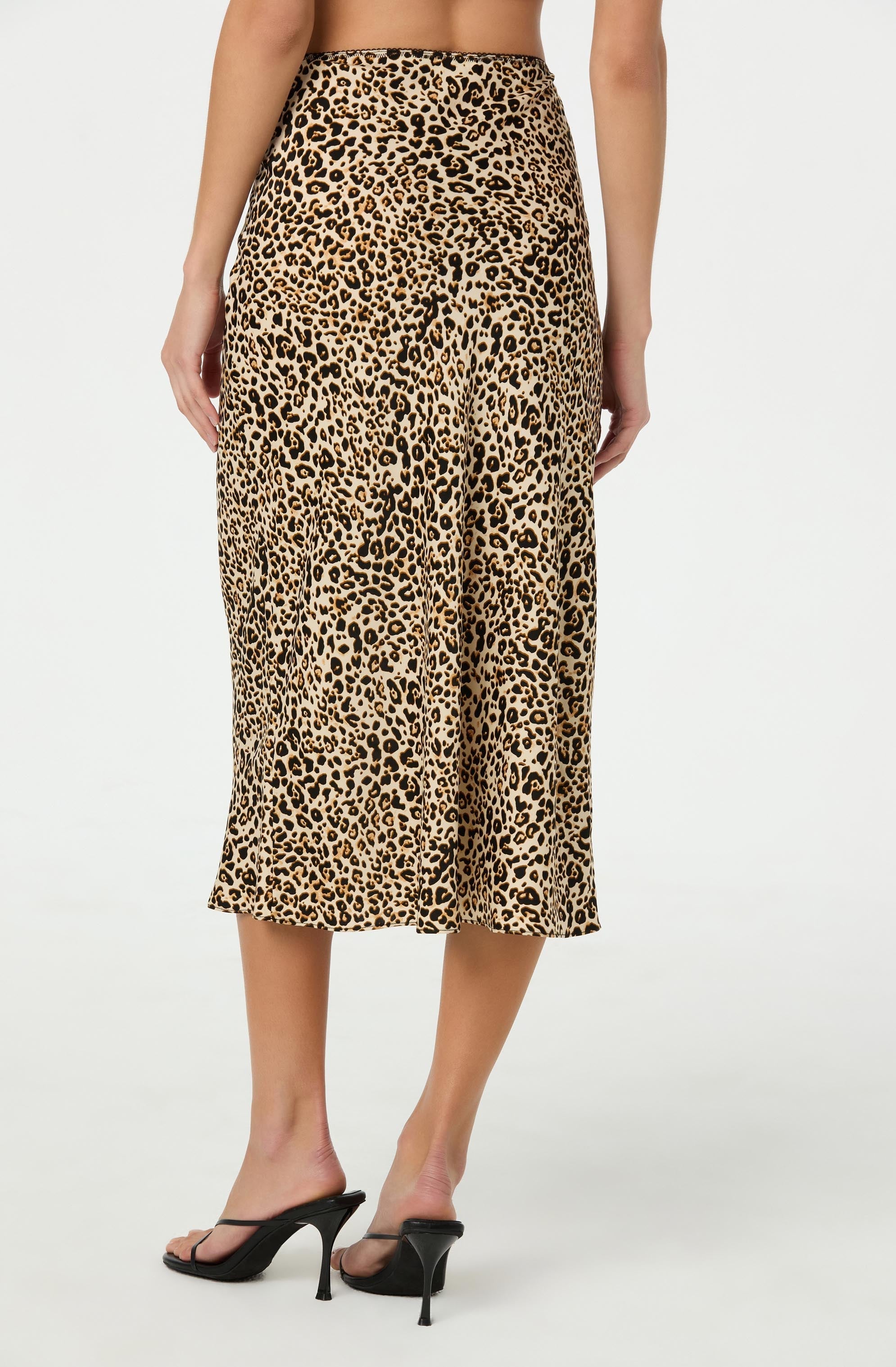 A woman is wearing a pair of high-waisted, midi-length pants with a leopard print pattern in shades of tan, black, and brown. The pants are loose-fitting and flowy, with a wide waistband. She is also wearing black high-heeled sandals with thin straps.