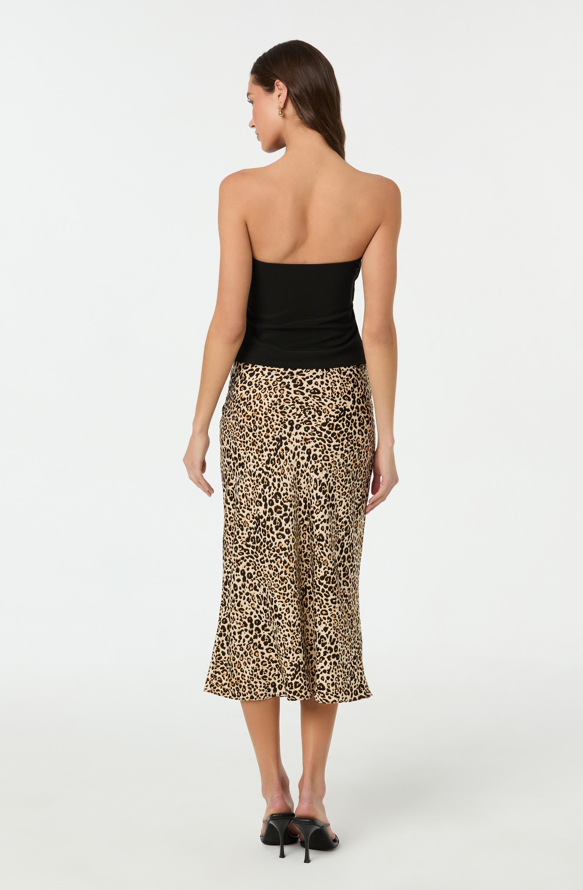 The woman is wearing a strapless black top and a high-waisted, ankle-length skirt with a leopard print pattern. She is also wearing black high-heeled shoes.