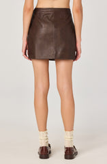 A person is wearing a dark brown leather mini skirt that has a smooth texture with visible stitching, paired with cream-colored knit socks and dark brown loafers.