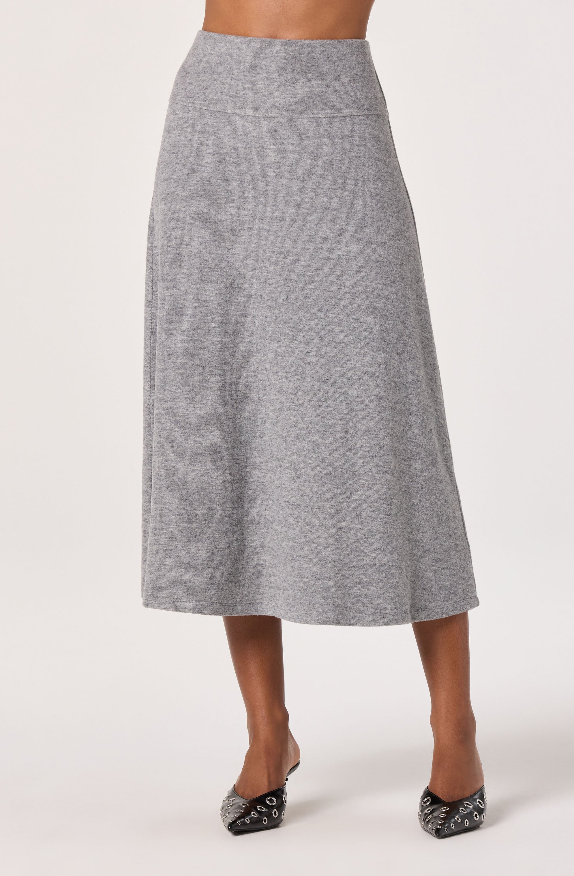 A woman is wearing a high-waisted, ankle-length, heather gray skirt made of a soft, knit fabric. She is also wearing black pointed-toe shoes with silver eyelet details.
