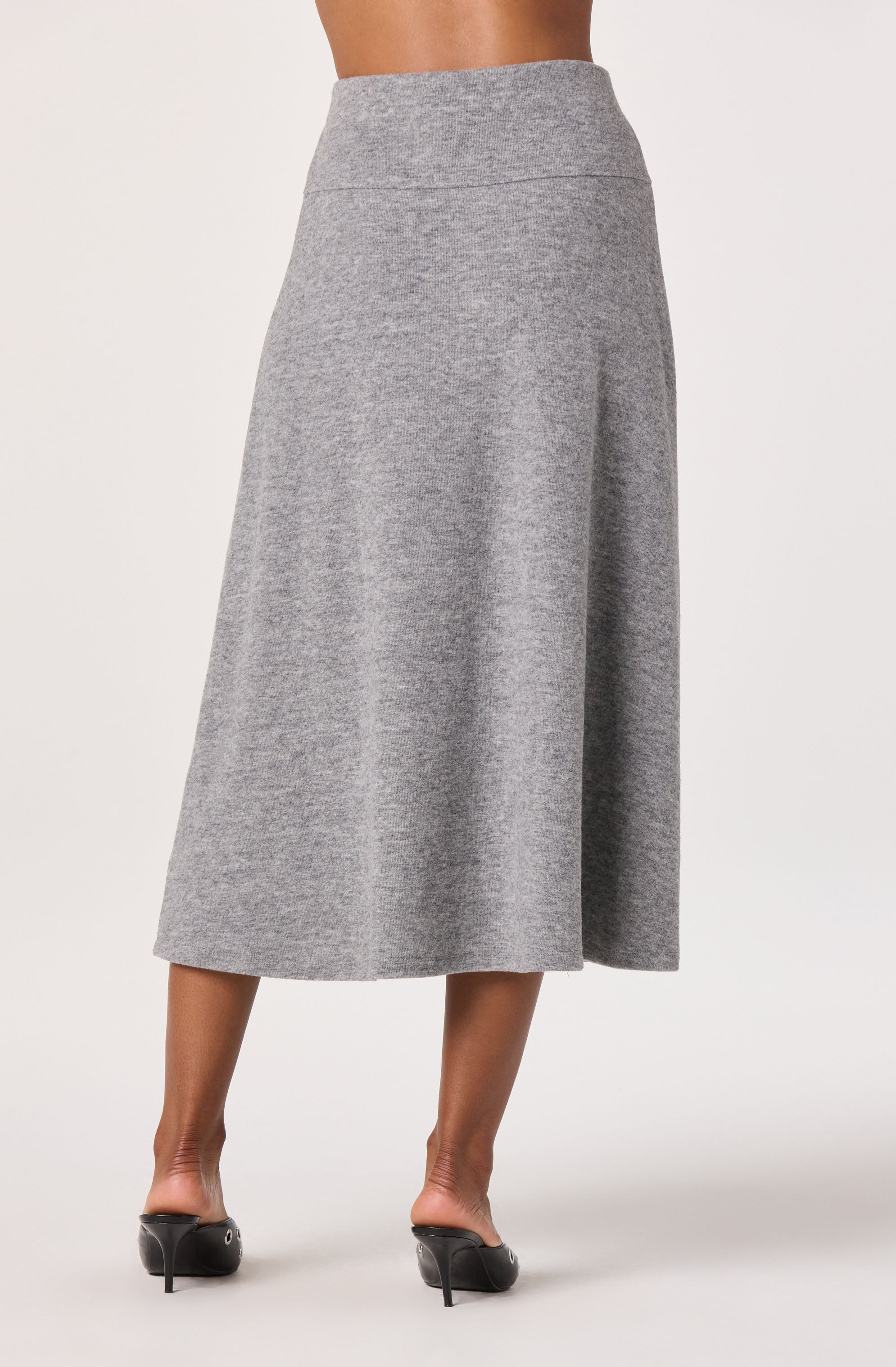 A woman is wearing a high-waisted, ankle-length gray skirt made of a soft, knit fabric. The skirt features a simple, clean design with a smooth waistband and no visible embellishments. She is also wearing black high-heeled shoes.