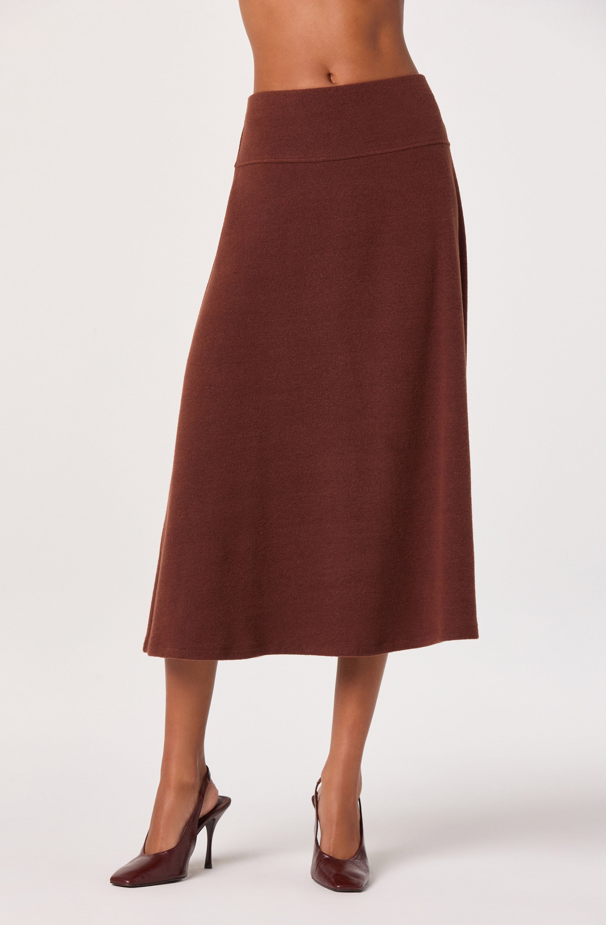 A woman is wearing a high-waisted, ankle-length brown skirt with a slightly flared hem. She is also wearing pointed-toe high heels in a matching brown color.