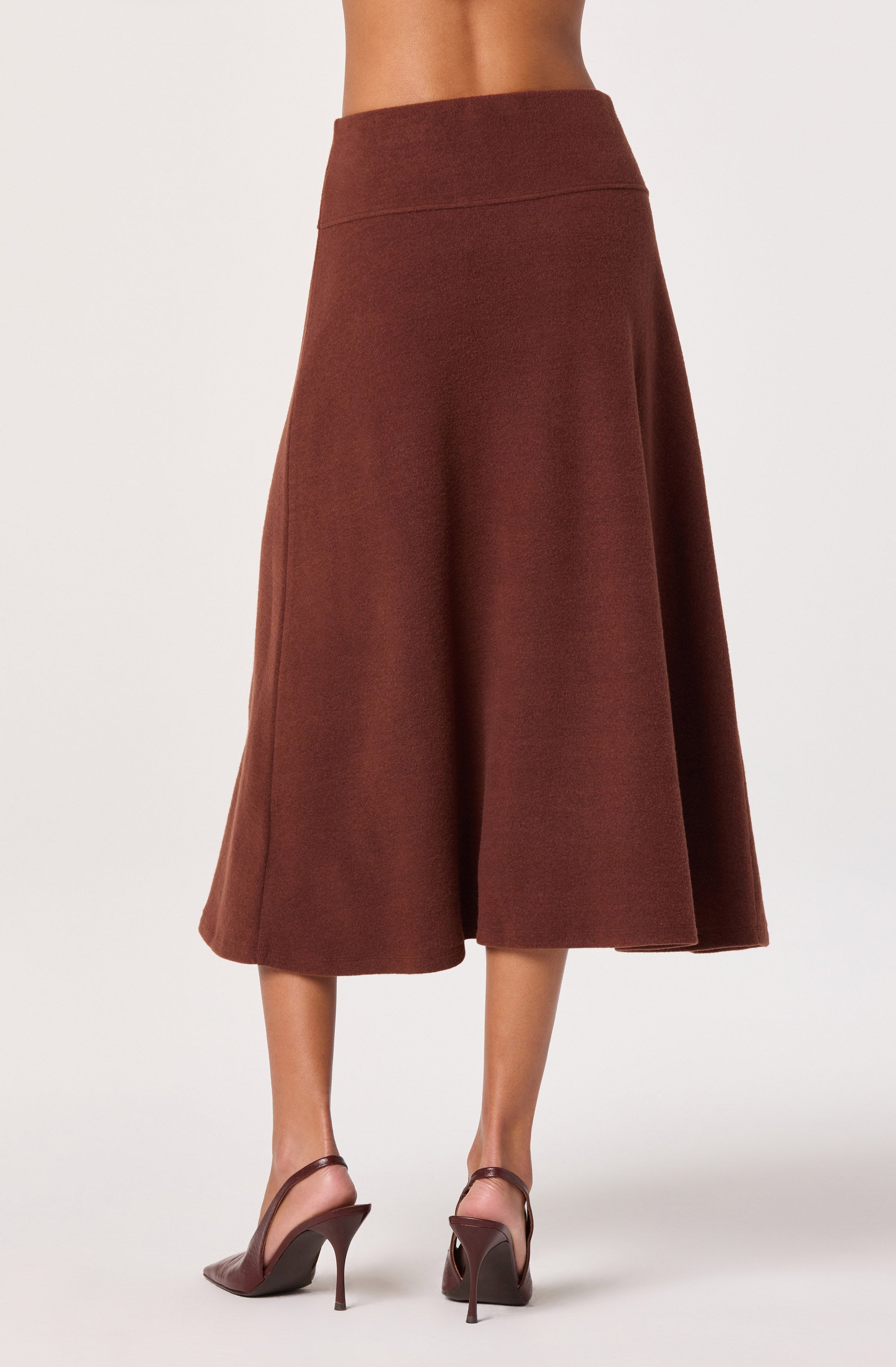 A woman is wearing a high-waisted, ankle-length brown skirt with a textured fabric. The skirt has a wide waistband and a subtle flare. She is also wearing brown high-heeled sandals with ankle straps.