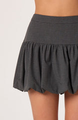 A high-waisted skirt with a small checkered pattern in black and gray. The skirt has a wide waistband and a ruffled, gathered hem that flares out.