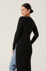 A woman wearing a long black ribbed knit sweater dress with a high neckline. The dress fits snugly and extends down past her knees. She pairs it with light blue high-waisted jeans.