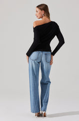 A woman is wearing a black off-the-shoulder sweater with long sleeves and light blue, high-waisted, wide-leg jeans. She has on white high-heeled shoes and is accessorized with statement earrings. She is standing against a plain, light background.