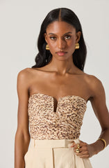 A woman is wearing a strapless top with a leopard print pattern and a center slit detail. She pairs it with high-waisted, light-colored pants. She accessorizes with large gold hoop earrings, a gold bracelet, and multiple gold rings.