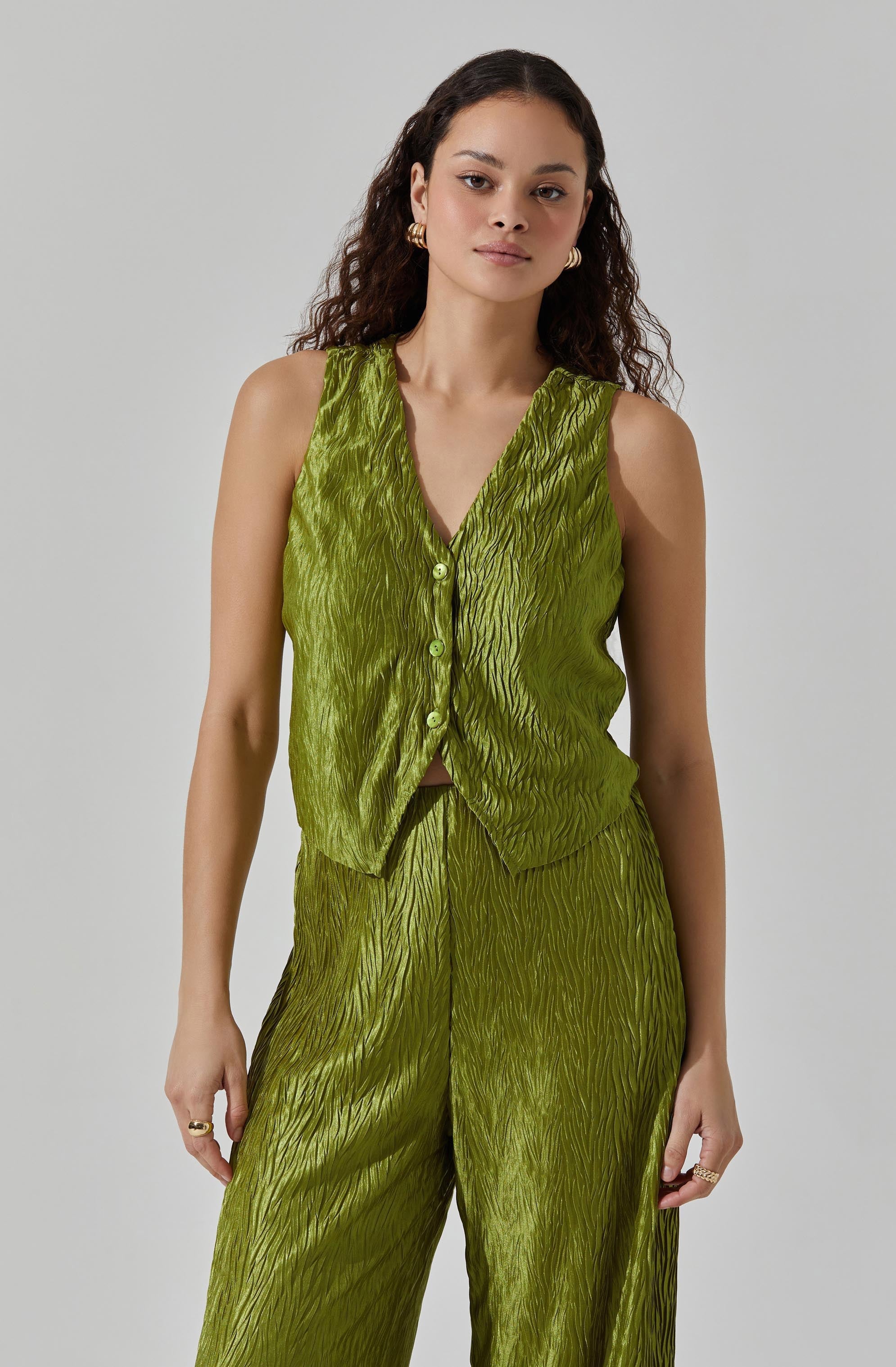 A woman is wearing a sleeveless, button-up top and matching wide-leg pants, both in a shiny, textured fabric with a crinkled appearance in a vibrant lime green color.
