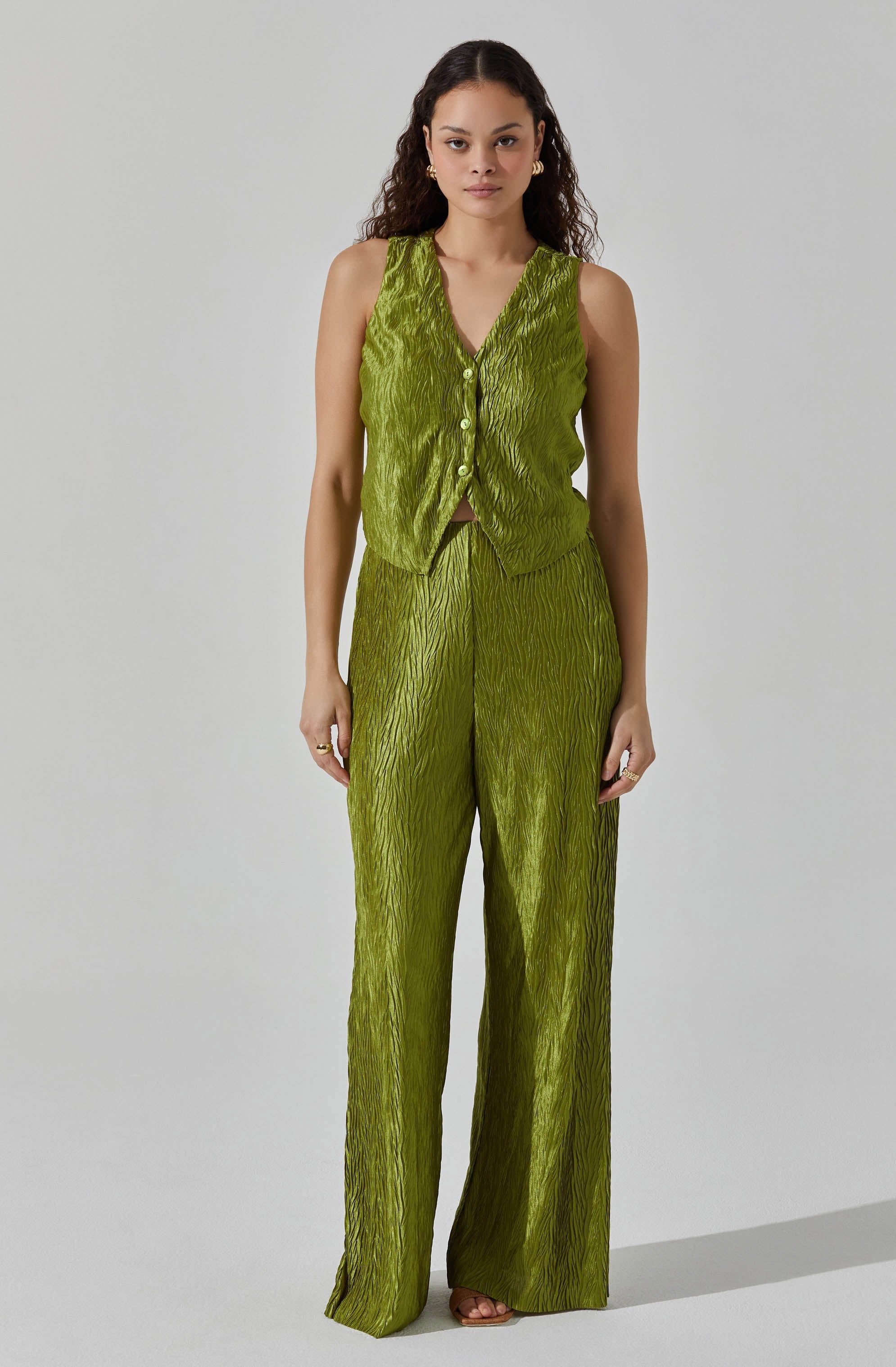A woman is wearing a shiny, textured, sleeveless vest and matching high-waisted, wide-leg pants in a bright green color.