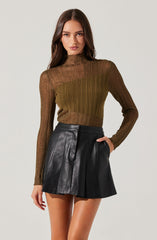 A young woman is wearing a long-sleeved, high-neck sweater with a gradient of brown and green shades and vertical ribbing details. She pairs it with a high-waisted black leather skirt that has a slight flare and pleats, with visible stitching and a front seam.