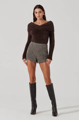 A woman is wearing a brown, off-the-shoulder, long-sleeve sweater that appears to be made of a fuzzy, textured material. She pairs it with high-waisted, gray, tweed shorts. Her outfit is completed with knee-high black leather boots.