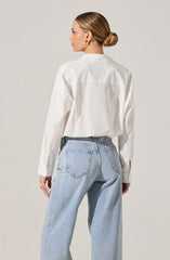 A woman is wearing a loose-fitting, long-sleeved white button-up shirt with a collar. The shirt has a slightly cropped length, ending just above the waist. She is also wearing light-wash, high-waisted jeans with a relaxed fit, featuring classic back pockets and visible stitching.