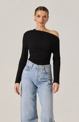 A woman is wearing a black, off-the-shoulder long-sleeve top paired with light-wash, high-waisted jeans. The top has a textured knit appearance and covers one shoulder while exposing the other. The jeans have a classic five-pocket design.