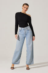 The woman is wearing a black, off-the-shoulder sweater with a loose fit, featuring long sleeves and a layered, textured design across the chest. She pairs it with high-waisted, light-wash wide-leg jeans that have a relaxed fit and a classic five-pocket style. She completes the outfit with black open-toe heels.