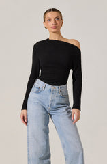 A woman is wearing a black, long-sleeved, off-the-shoulder top with a textured fabric, paired with high-waisted, light-wash jeans.