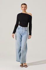 A woman is wearing a black, off-the-shoulder long-sleeve top paired with light-wash, high-waisted wide-leg jeans. She is also wearing black strappy high-heeled sandals.