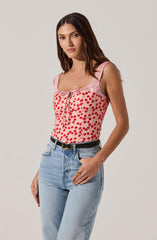 A woman is wearing a sleeveless pink top with a cherry print design and a small bow at the neckline. She pairs it with light blue high-waisted jeans and a black belt.