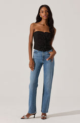 A woman is wearing a strapless black top with ruffled details down the front, paired with high-waisted blue jeans. She is also wearing open-toe high heels with a decorative bow on the front.