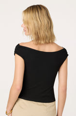 A woman is wearing a black, short-sleeved top with a wide, slightly off-the-shoulder neckline. The top fits snugly and is made of a smooth fabric. She is also wearing a beige skirt.