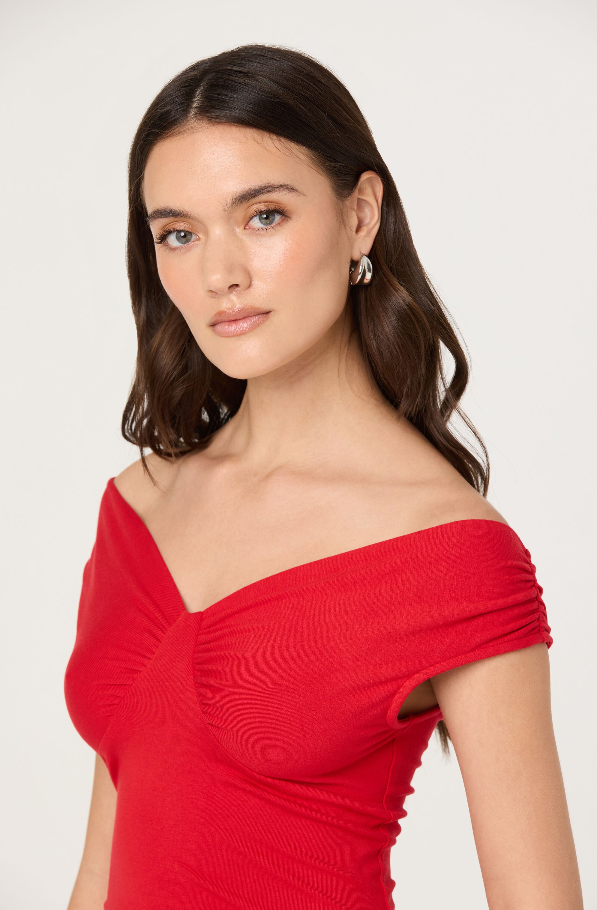 A woman is wearing a fitted, off-the-shoulder red dress with gathered detailing along the sleeves and bust.