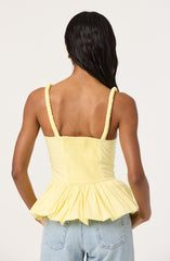 A woman is wearing a sleeveless yellow top with ruffled shoulder straps and a smocked bodice, featuring a peplum-style gathered hem. She is also wearing light blue jeans.