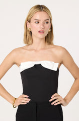 The woman is wearing a strapless black top with a large white bow detail across the chest.