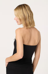 A woman with shoulder-length blonde hair is wearing a strapless black top and black pants.