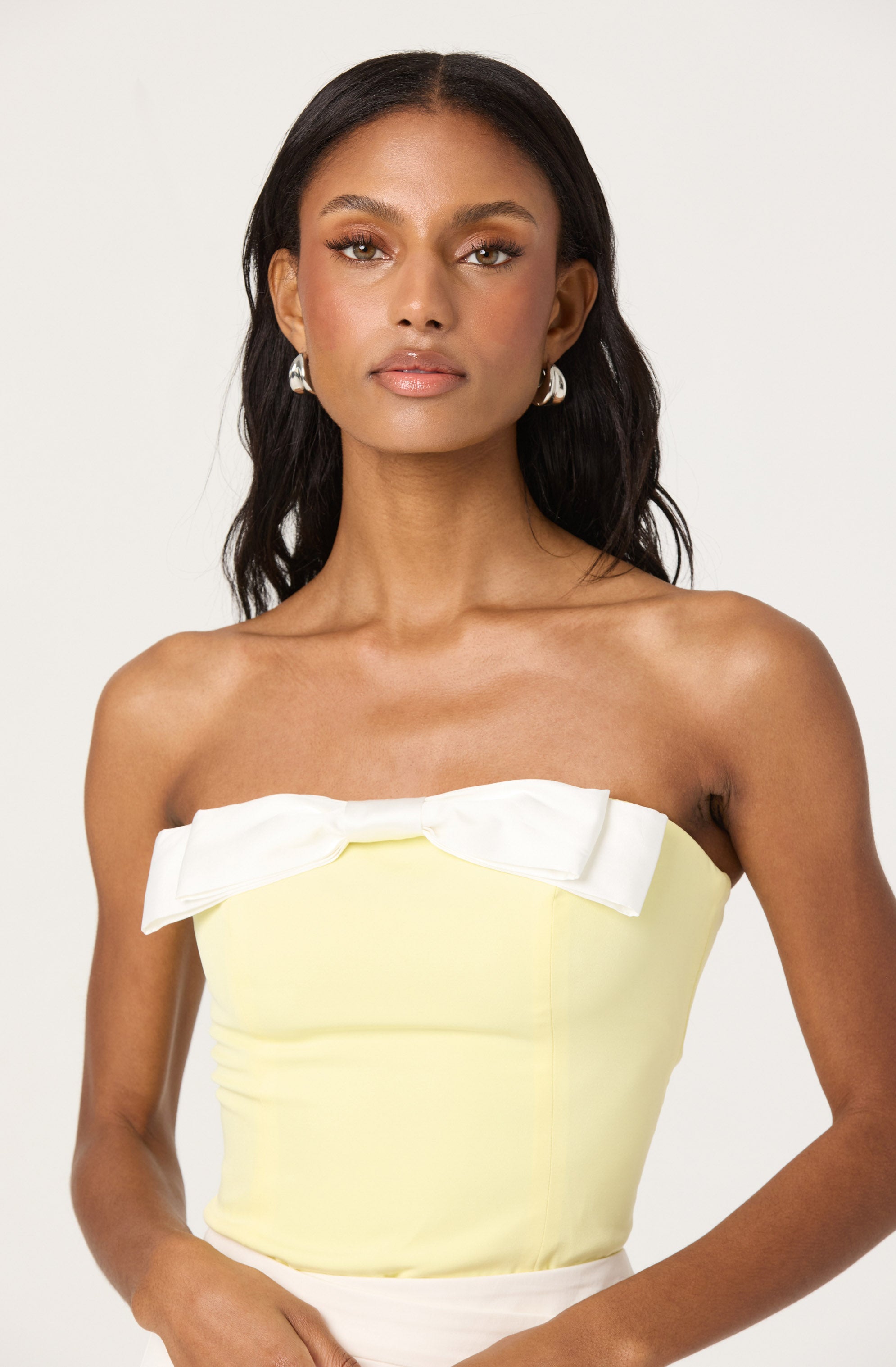 A woman is wearing a strapless, pale yellow top with a large white bow across the chest.