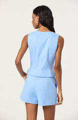 A woman is wearing a sleeveless, light blue top and matching shorts. The top has a round neckline and a slightly cropped length. The shorts are high-waisted with a tailored fit. The outfit appears to be made of a lightweight fabric suitable for warm weather.