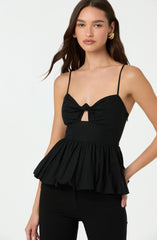 A woman is wearing a black sleeveless top with thin spaghetti straps. The top features a gathered bust with a decorative bow at the center and a small keyhole opening below the bow. The waist is fitted, and the garment has a ruffled, peplum-style hem that extends outward.