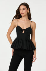 A woman is wearing a black sleeveless top with thin spaghetti straps. The top features a bustier style with a knot detail and a small cutout below the knot. It has a gathered, ruffled peplum hem that flares out at the waist.