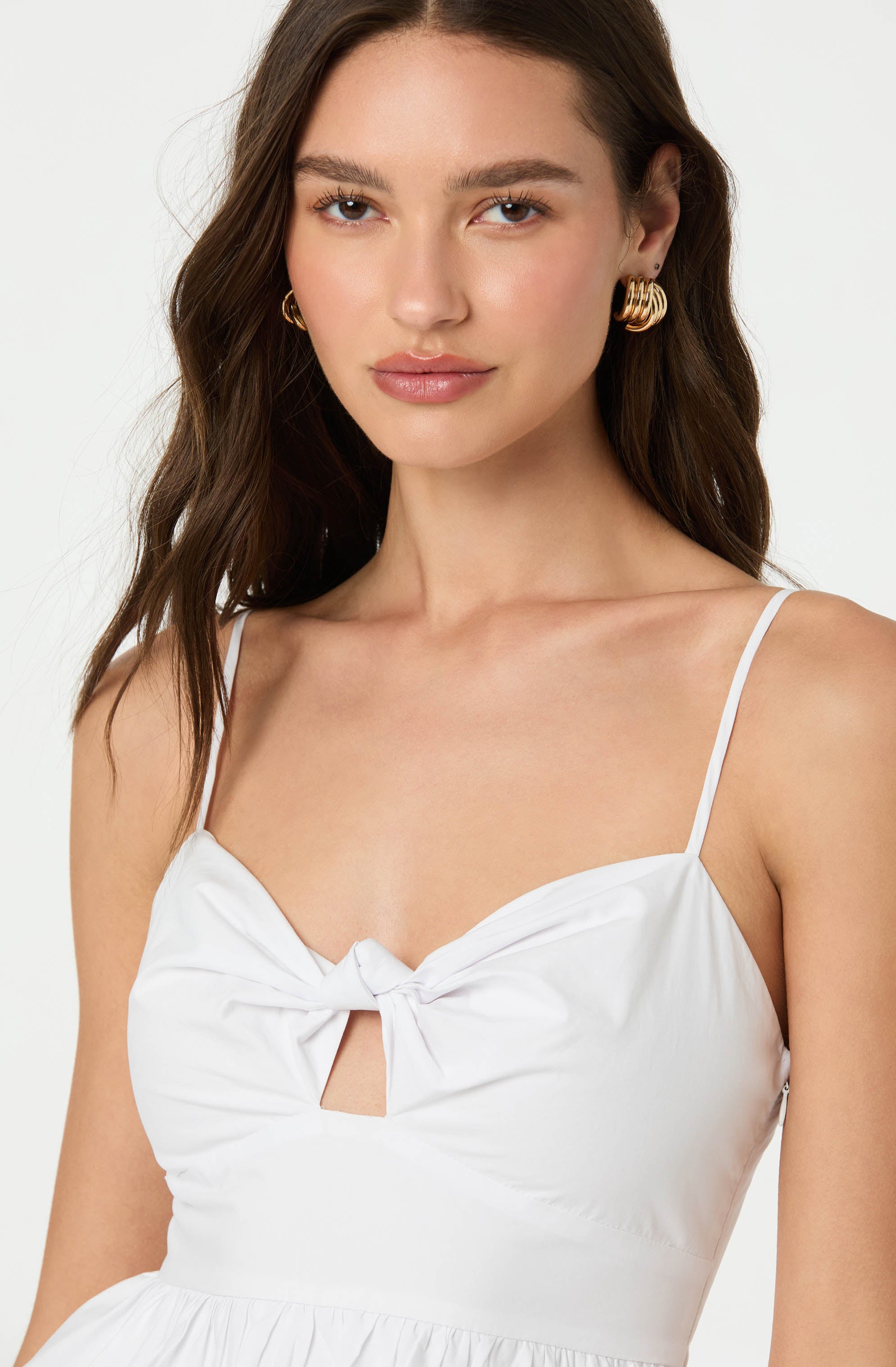 A woman wearing a white dress with spaghetti straps, featuring a front knot detail and a small keyhole cutout just below the knot.