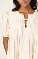 A woman is wearing a cream-colored dress with vertical pinstripes. The dress features a rounded neckline and has two small bows at the front near a keyhole opening. The fabric appears lightweight and flowing, with gathered puff sleeves.