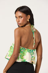 A woman is wearing a sleeveless, halter top with a tie at the back of the neck. The top features a colorful, abstract floral pattern in shades of green, pink, yellow, and black on a light background.
