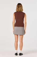 A woman is wearing a sleeveless, brown knit vest paired with a short, gray and white checkered skirt. She has on white socks and black shoes. Her hair is shoulder-length and light brown.