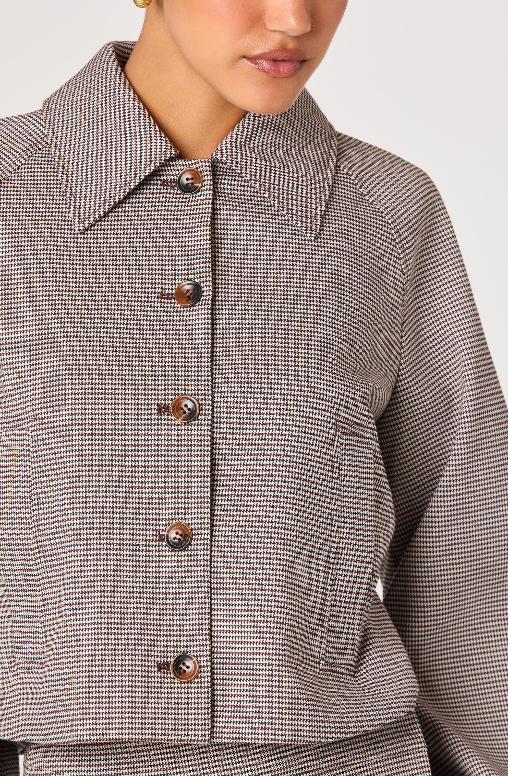 A woman wearing a long-sleeved button-up shirt with a small checkered pattern in shades of brown, black, and white. The shirt features a pointed collar and brown buttons down the front.