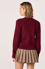 A person is wearing a maroon, long-sleeved, knitted sweater with a crew neckline. They are also wearing a pleated skirt with a beige and black checkered pattern.